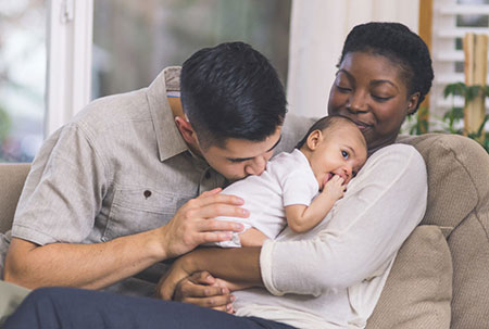 Interracial couple kiss their adopted baby
